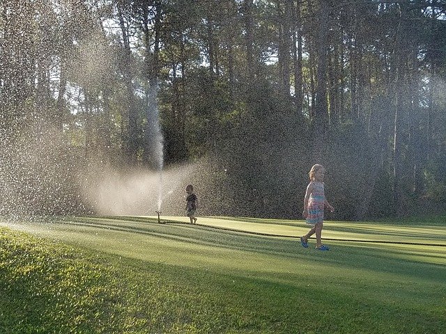 A nicely cut lawn being watered with a sprinkler